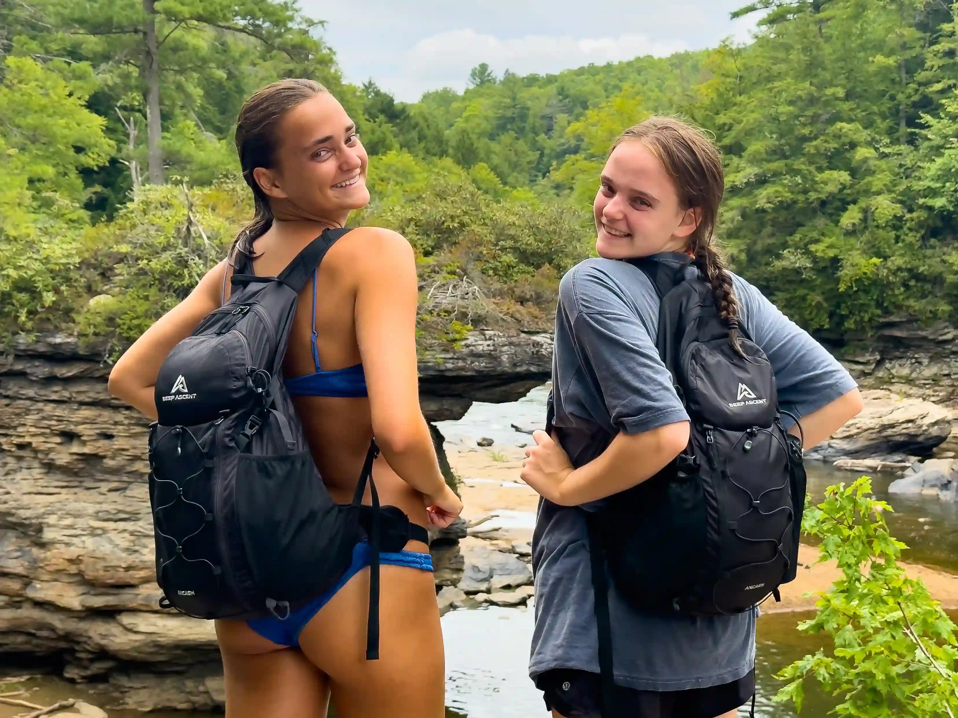 Two women standing in front of a creek in Maryland's Swallow Falls State Park, each wearing the Ancash Packable Daypack by Deep Ascent.