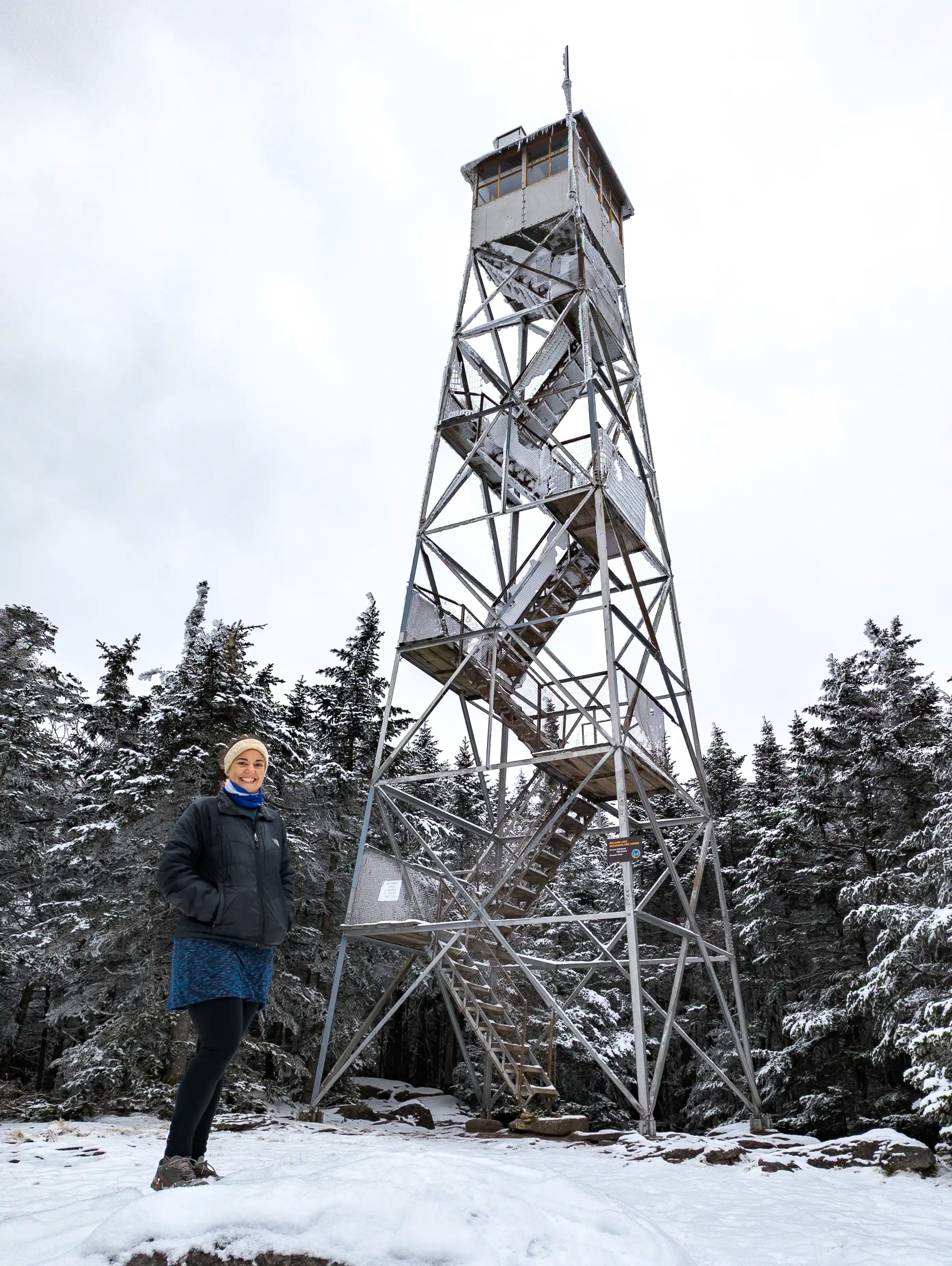 A female standing in front of Balsam Lake Mountain fire tower in New York.