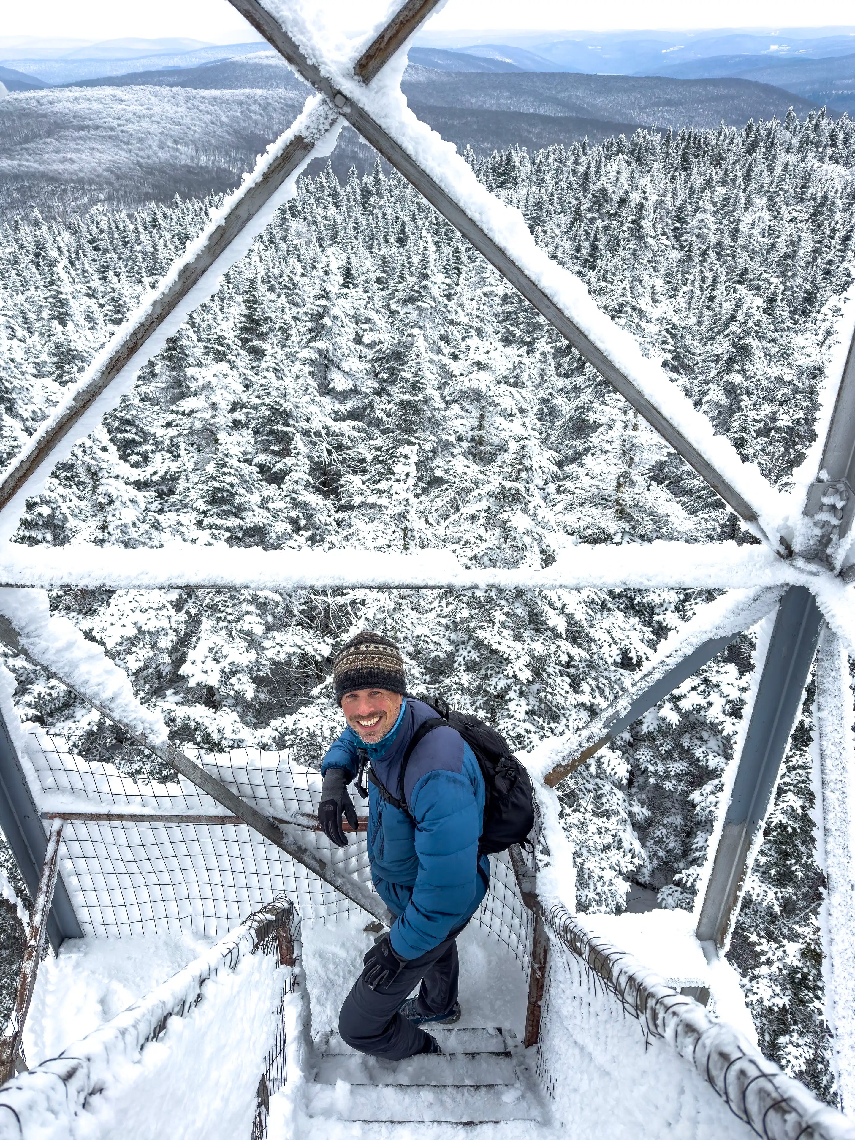 A man standing on the Balsam Lake Mountain fire tower in New York wearing the Ancash Packable Daypack by Deep Ascent.