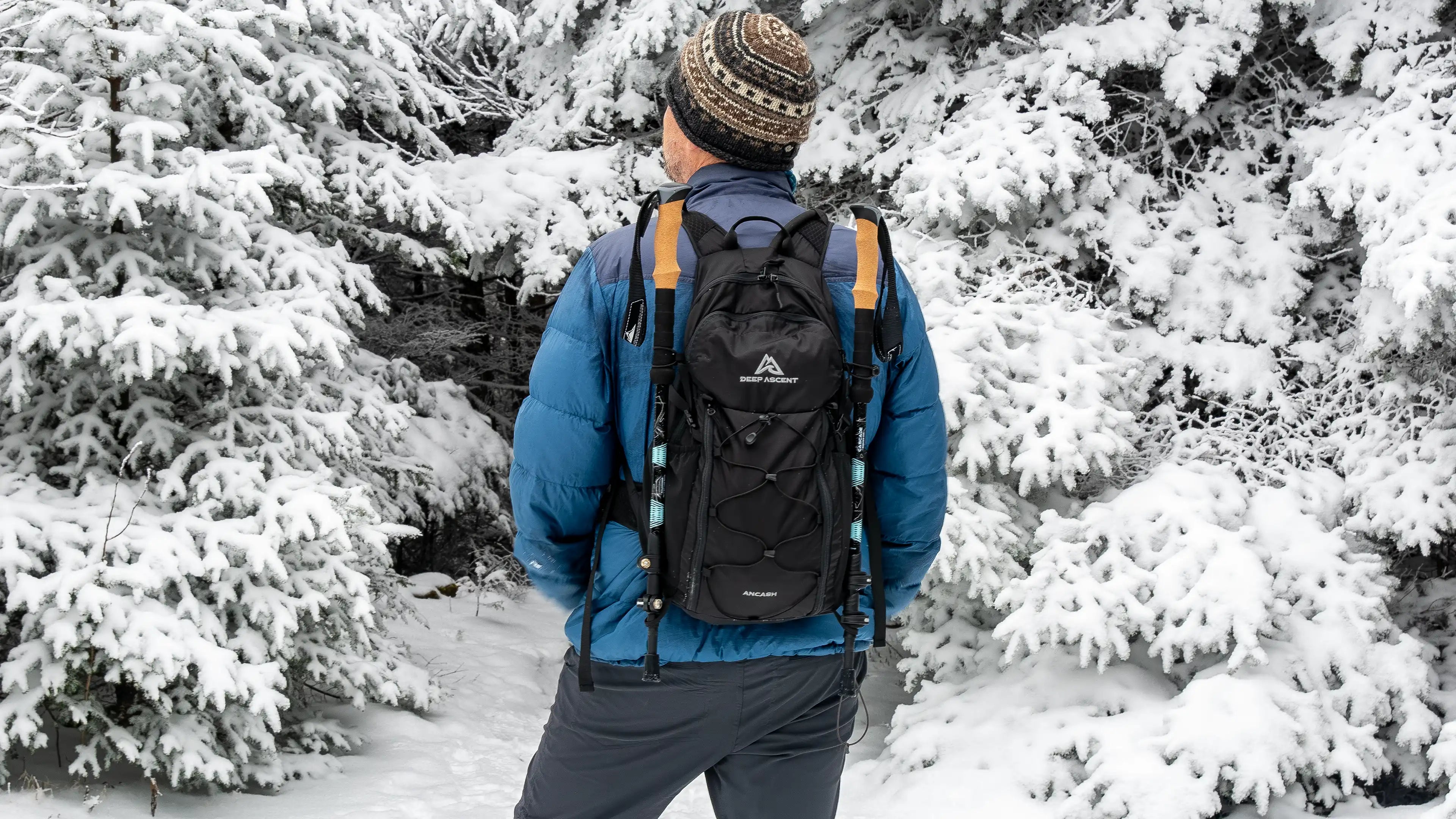 Hiker wearing the Ancash Packable Daypack with trekking poles attached, standing in front of snow-covered trees on the summit of Balsam Lake Mountain in New York.