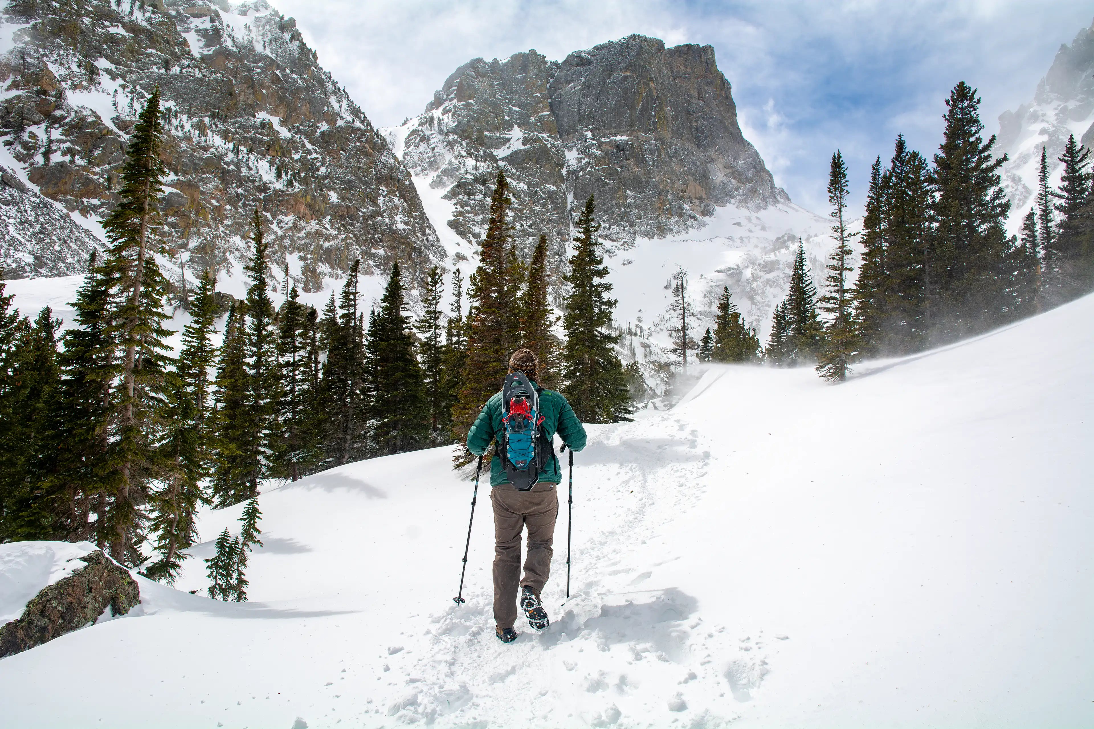 Hiker wearing the Ancash Packable Daypack with snowshoes mounted, on a snow-packed Emerald Lake Trail in Rocky Mountain National Park.