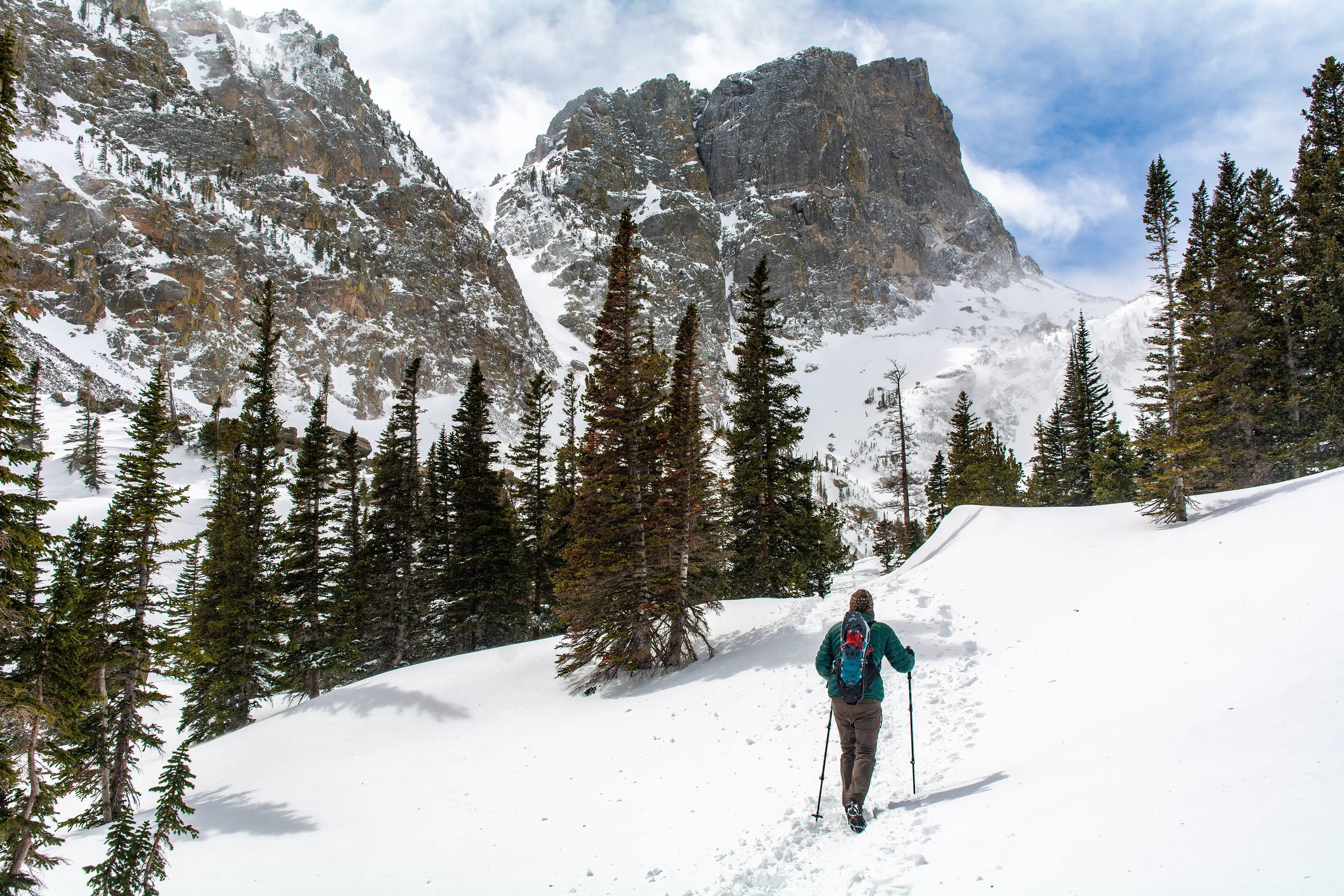 Hiker wearing the Ancash Packable Daypack with snowshoes mounted, on a snow-packed Emerald Lake Trail in Rocky Mountain National Park.