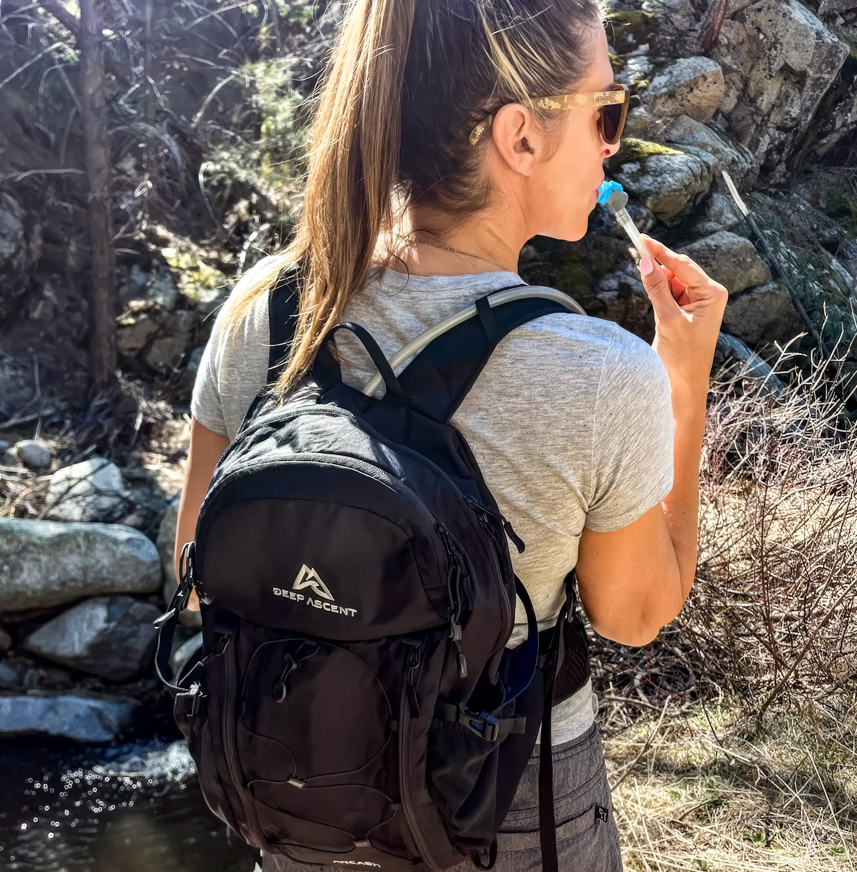 A woman using the hydration feature of the Ancash Packable Daypack by Deep Ascent.