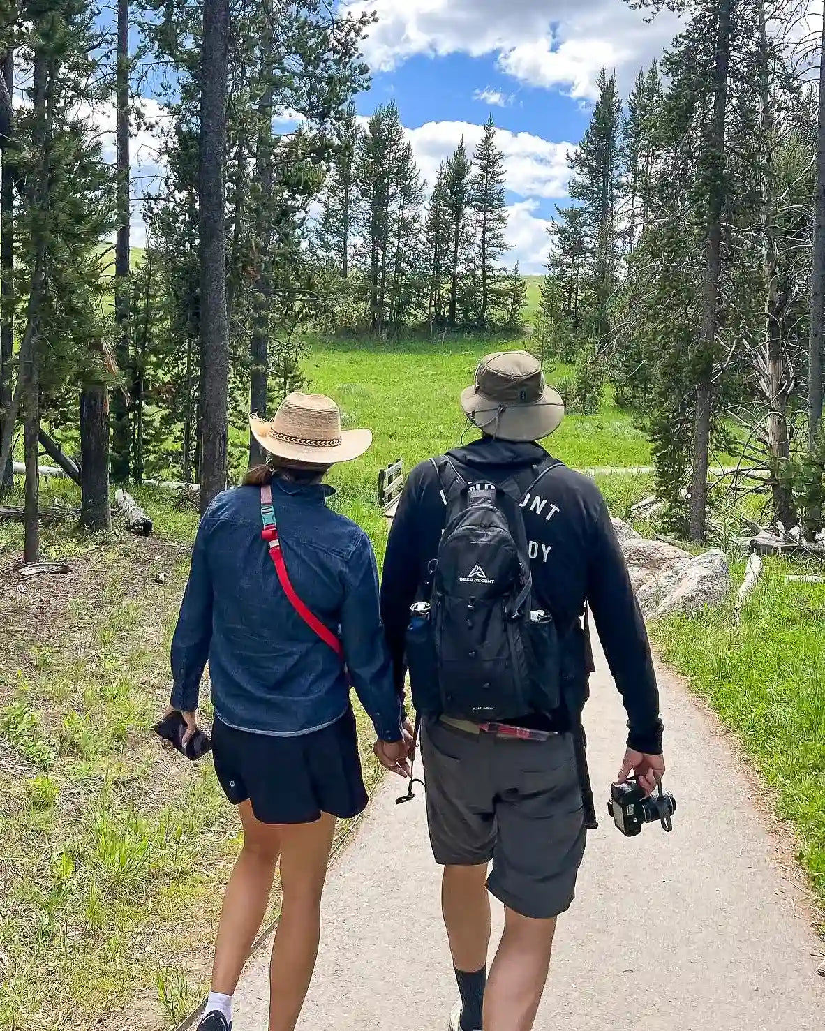 Couple holding hands walking on a trail in Yellowstone National Park, with one wearing the Ancash Packable Daypack by Deep Ascent.