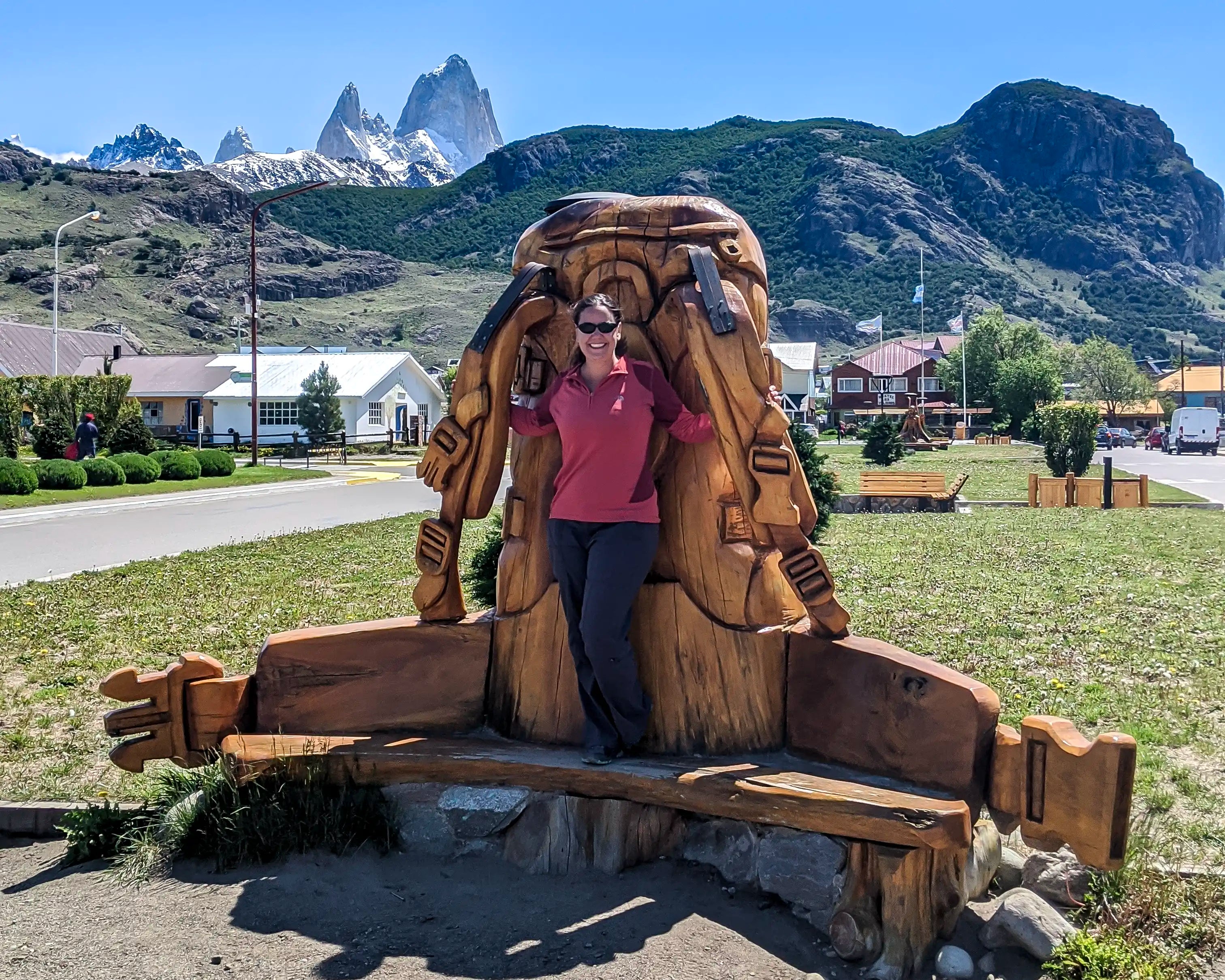 A woman standing on a wooden park bench sculpture of a backpack in El Chaltén, Argentina.