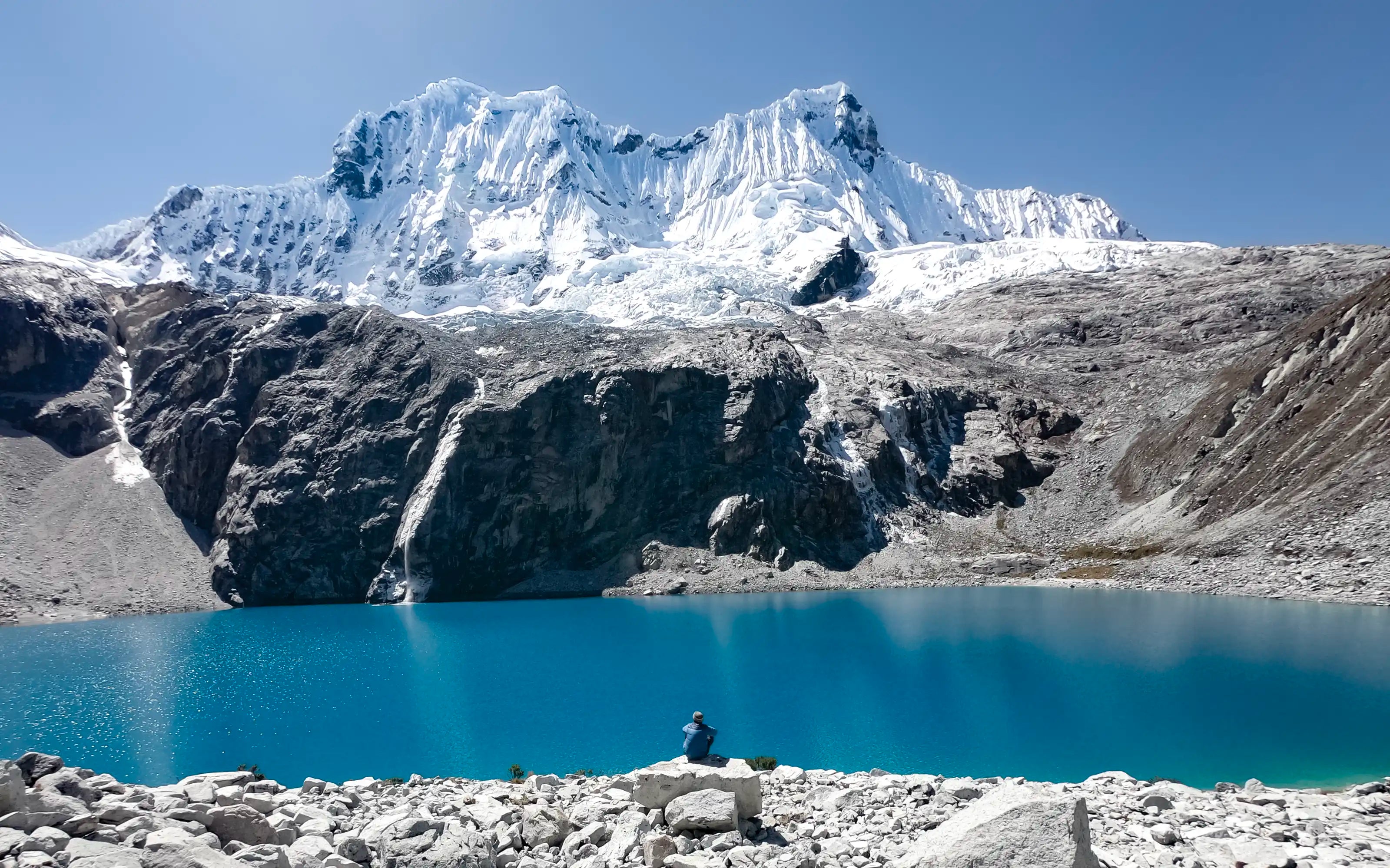 A man sitting on a rock in front of Laguna 69 in Peru.