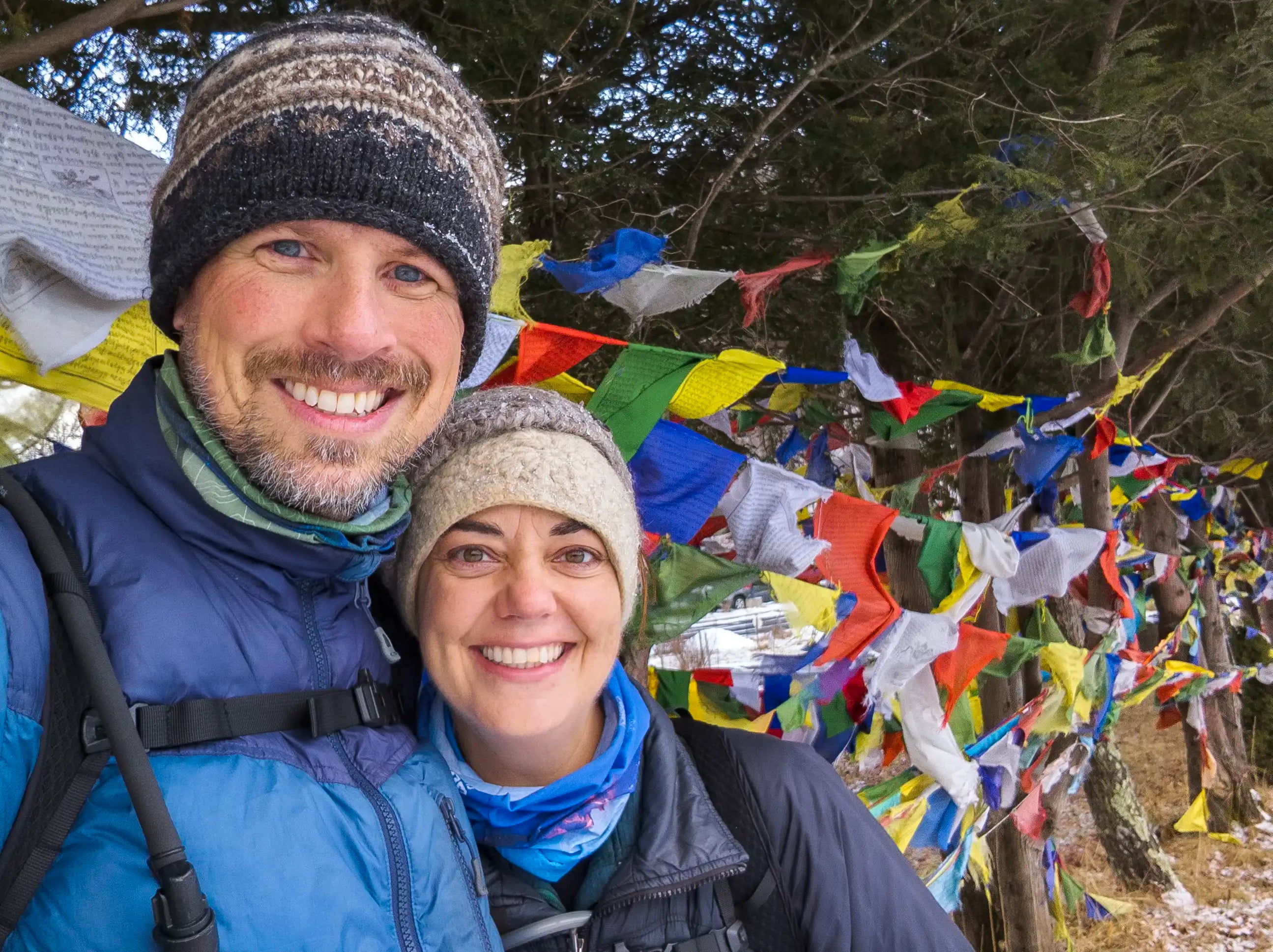 A man and woman standing next to Buddhist prayer flags attached to trees.