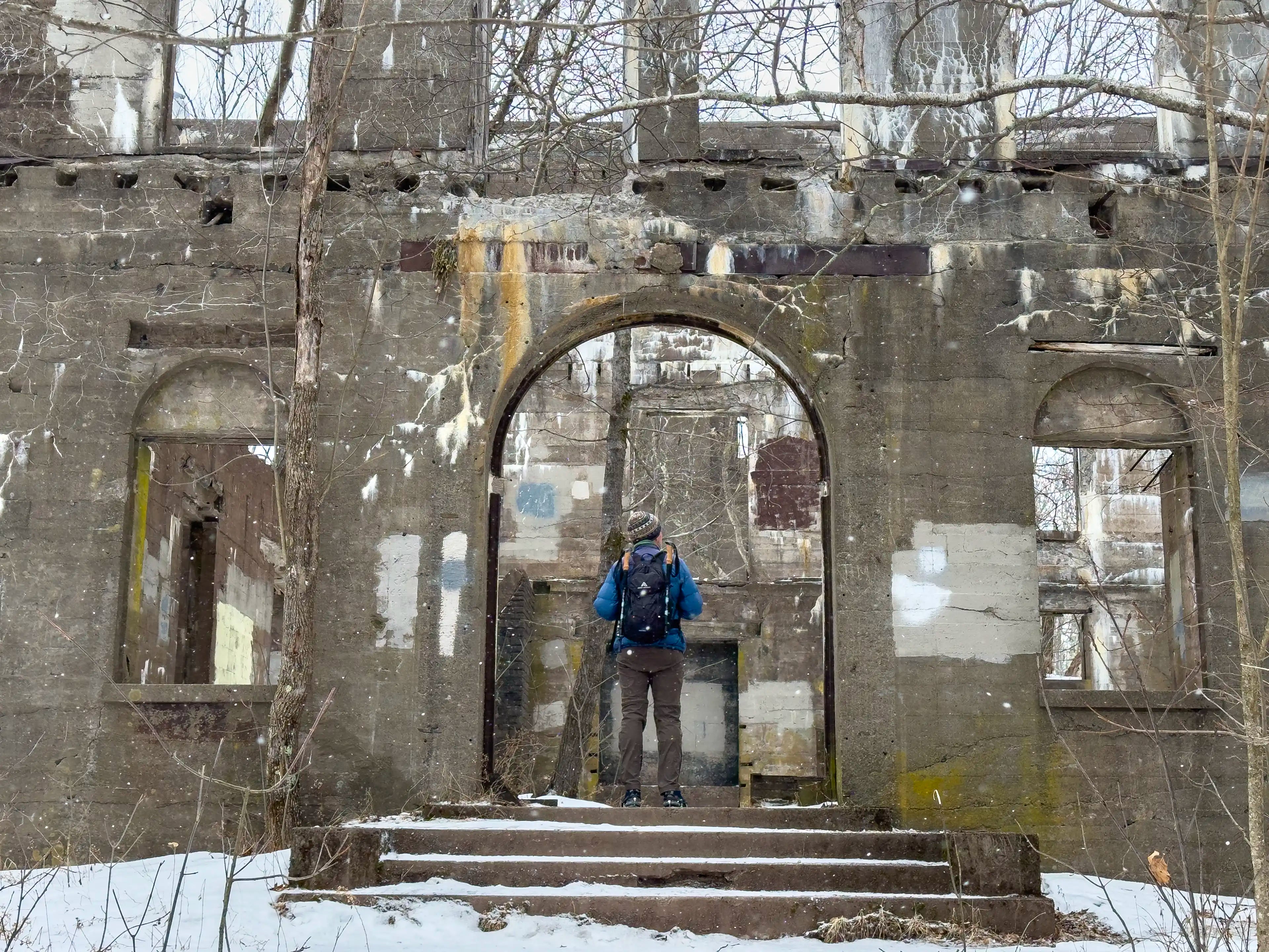 A male hiker standing at the entrance of an abandoned hotel on Overlook Mountain in New York wearing the Ancash Packable Daypack by Deep Ascent.