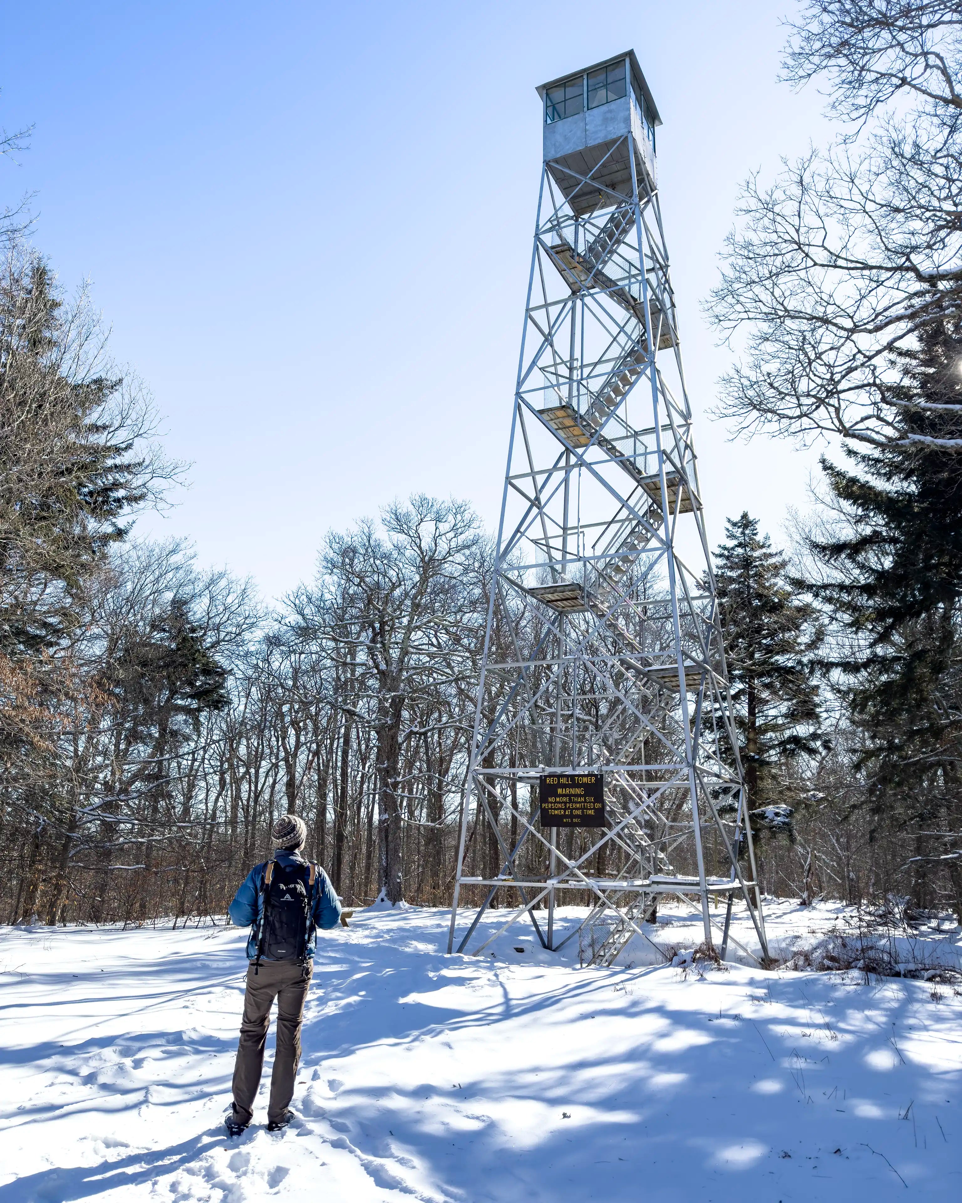 A male hiker standing in front of Red Hill Fire Tower in New York wearing the Ancash Packable Daypack by Deep Ascent.