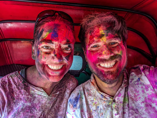 A man and woman sitting in a tuk tuk  in New Delhi, India covered in colored powder during Holi.